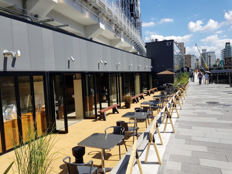 Tokyo Mizumachi waterfront cafe promenade with outdoor seating, tiled walkway, and E7 building.