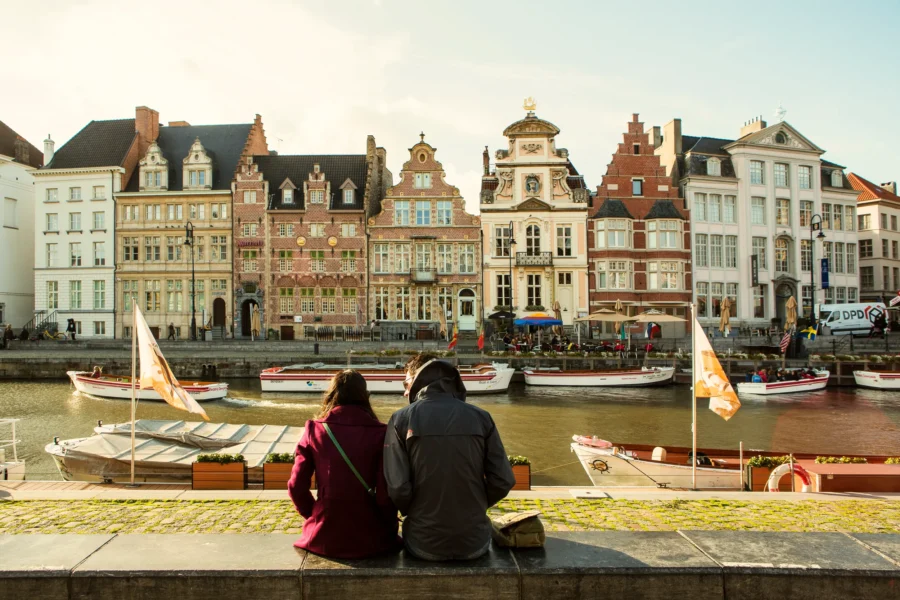 Romantic couple by historic European riverfront with colorful buildings and boats at sunset.