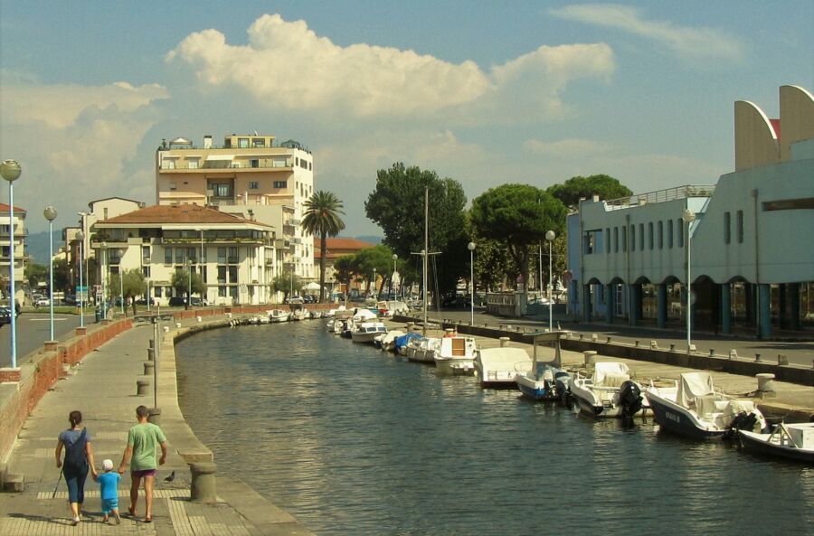 Serene Viareggio waterfront promenade with modern architecture, lush greenery, and peaceful family stroll.