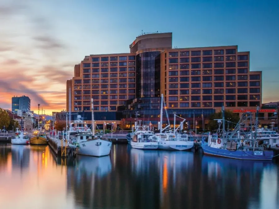 Harbor waterfront at twilight with modern hotel building, fishing boats, reflections, colorful sunset sky.