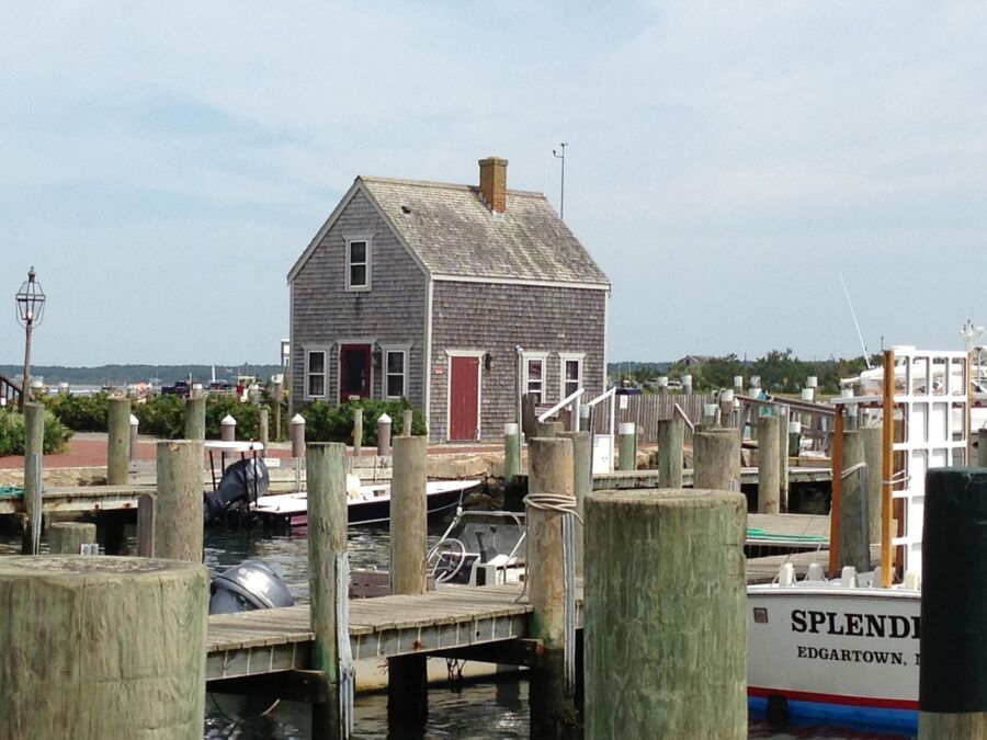 Charming Martha’s Vineyard harbor scene with quaint house, docked boats, sunny sky, and coastal views.