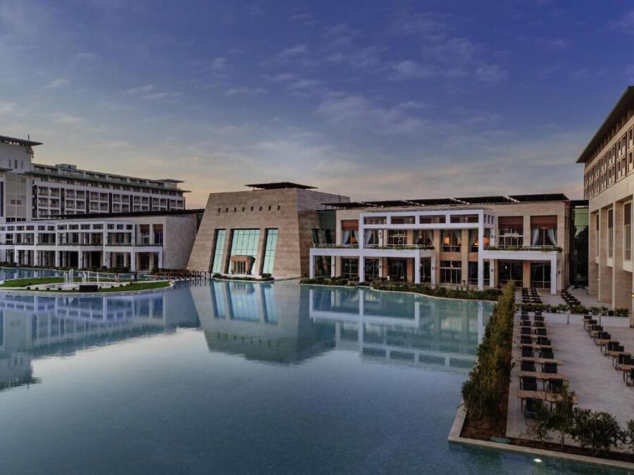 Luxury waterfront resort with modern architecture reflecting in calm lagoon pool at dusk.