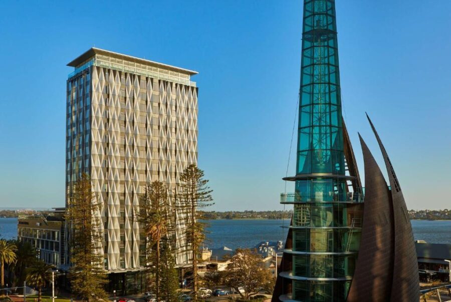 Modern Perth waterfront skyline with DoubleTree hotel, glass tower, pine trees and blue river.