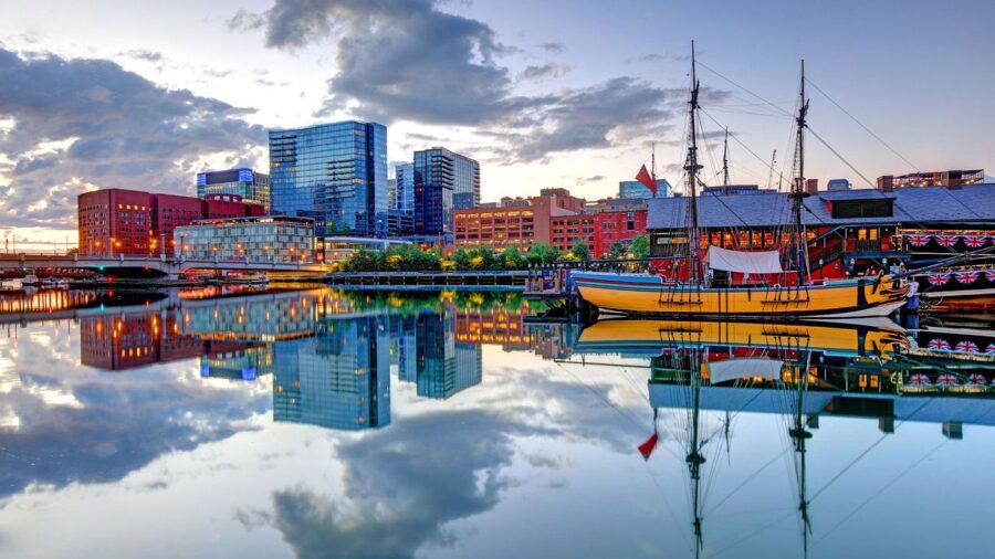 Bustling Boston Harbor at dusk, featuring a vibrant skyline and anchored yellow boat.