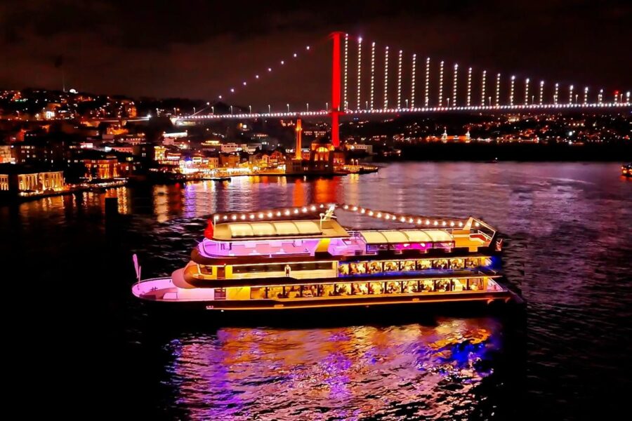 Illuminated dining boat on Bosphorus with Istanbul skyline and iconic bridge at night.