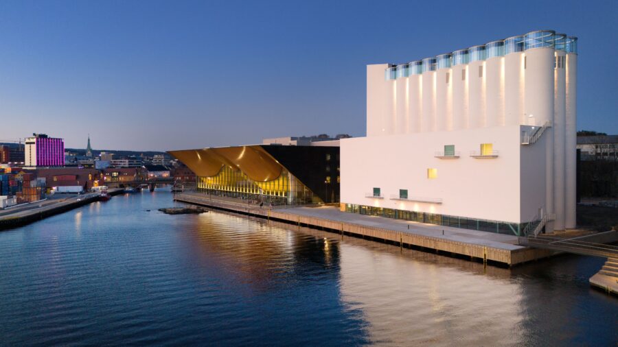 Kunstsilo waterfront at twilight: modern silos and glass building reflected on calm river.