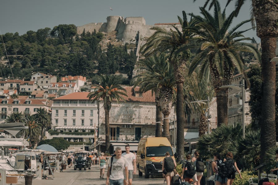 Hvar, Croatia waterfront promenade with palm trees, marina and Fortica fortress overlooking harbor.