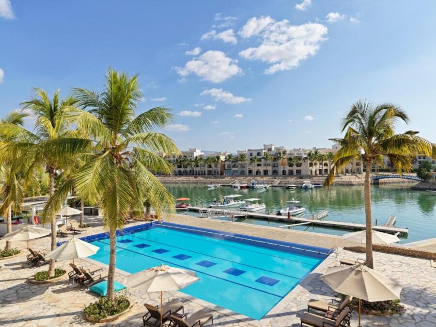 Luxury waterfront resort with turquoise pool, marina, palm trees and modern beachfront hotel buildings.
