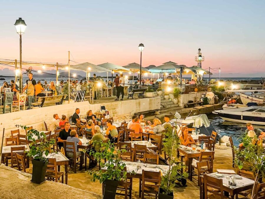 Waterfront dining in Chania harbor at sunset with bustling seaside restaurants and string lights.