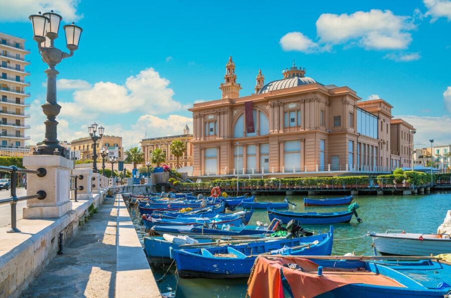 Picturesque Bari harbor with colorful boats, a historic building, and bright sky.
