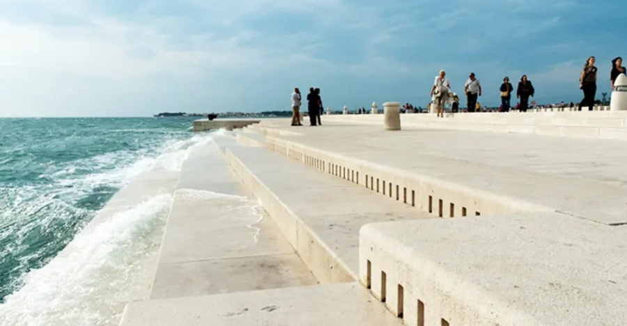 Modern waterfront promenade with concrete steps and scenic sea views, people relaxing.