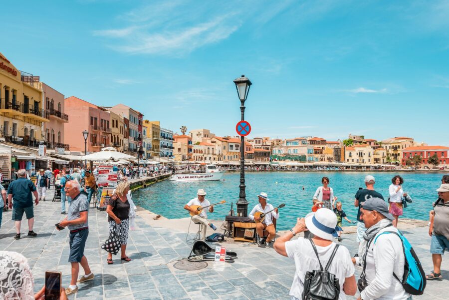 Mediterranean waterfront: tourists, musicians, colorful buildings, lively atmosphere, and scenic harbor.