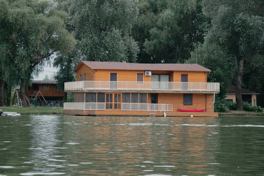 Lakeside wooden house with balcony, kayak, and tranquil forested surroundings.