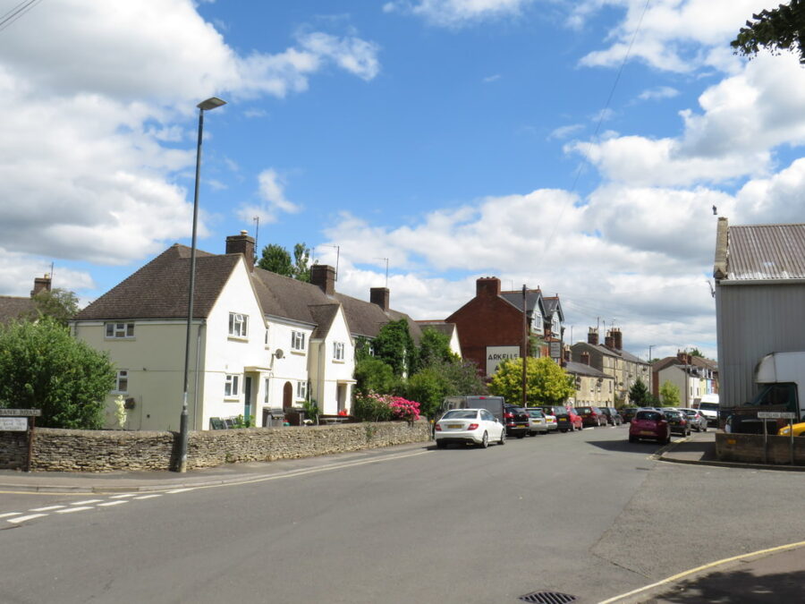 The sky is filled with clouds against a blue backdrop over Watermoor Road in Cirencester, evoking a tranquil scene.