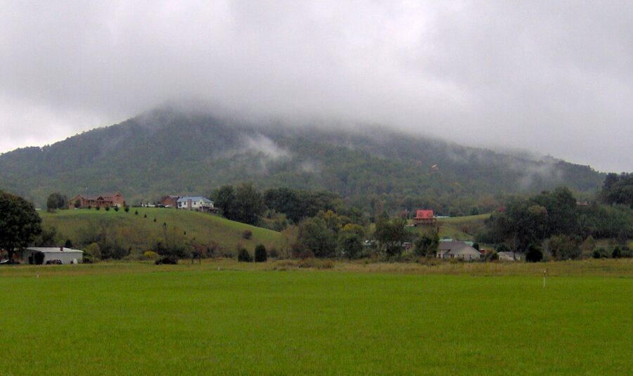 Scenic field in Wears Valley, Tennessee, with a distant house framed by rolling hills under a clear sky.