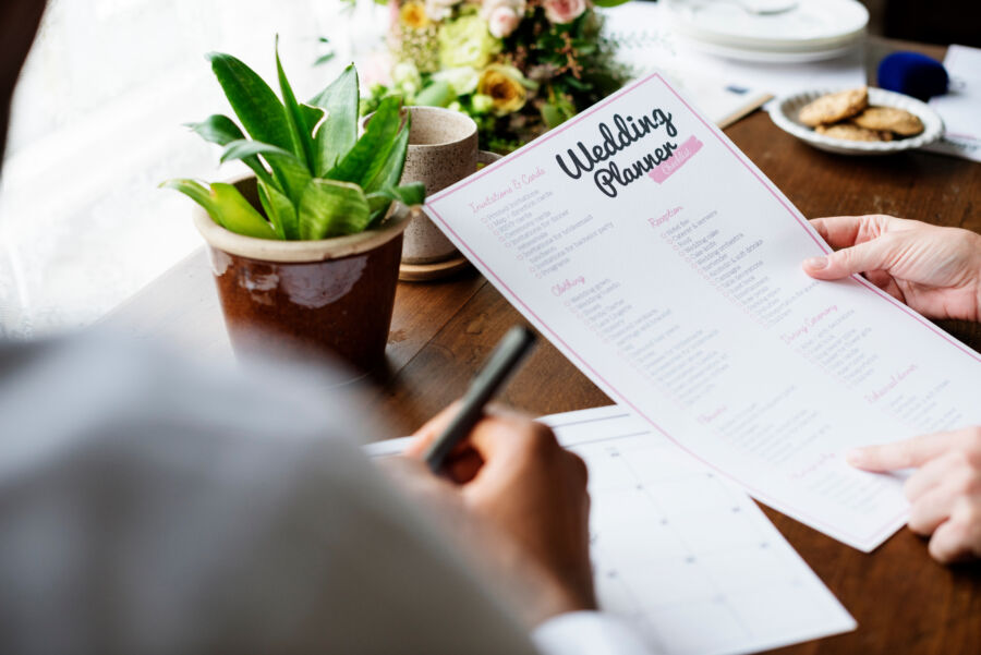 Hands holding a wedding planner checklist, showcasing preparation details for organizing a wedding event  
