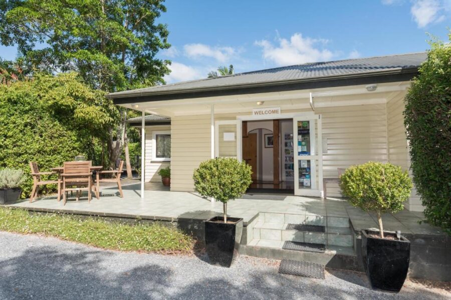 Welcoming motel reception entrance with outdoor seating, potted plants, tiled patio and lush greenery.