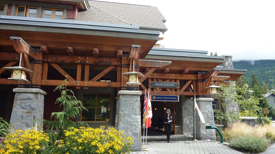 Whistler Railway Station, displaying a flag as he steps outside, with the station's facade in view.