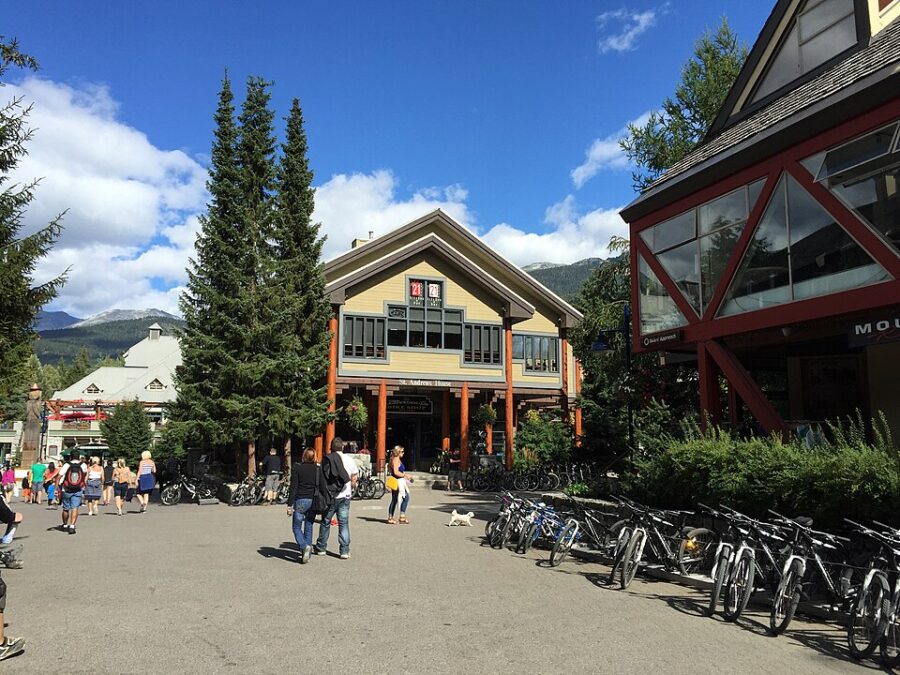 Group of people riding bicycles and walking through Whistler Village, surrounded by shops and scenic views.