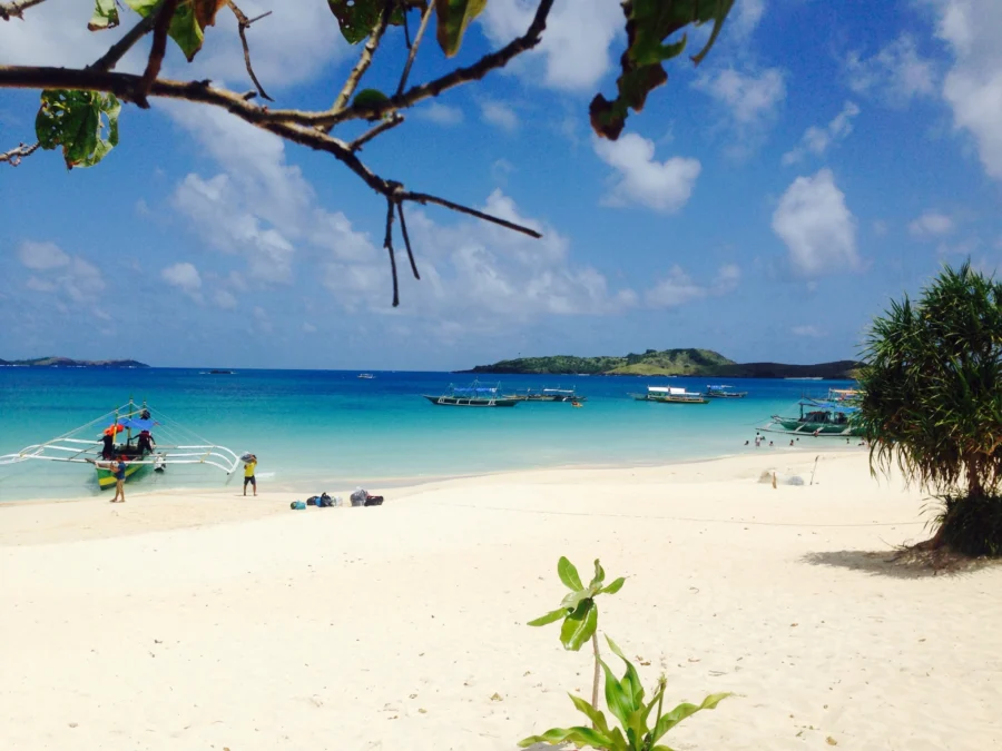 Calaguas white-sand beach with turquoise water, outrigger boats, tropical island.
