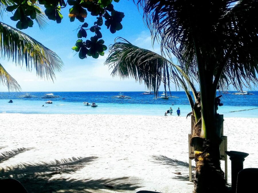Alona Beach Philippines white sand palm beach with turquoise water and boats.
