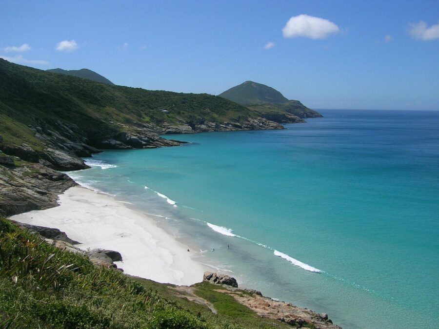 Secluded white sand beach with turquoise bay, green hills, clear blue sky, remote coastal paradise.