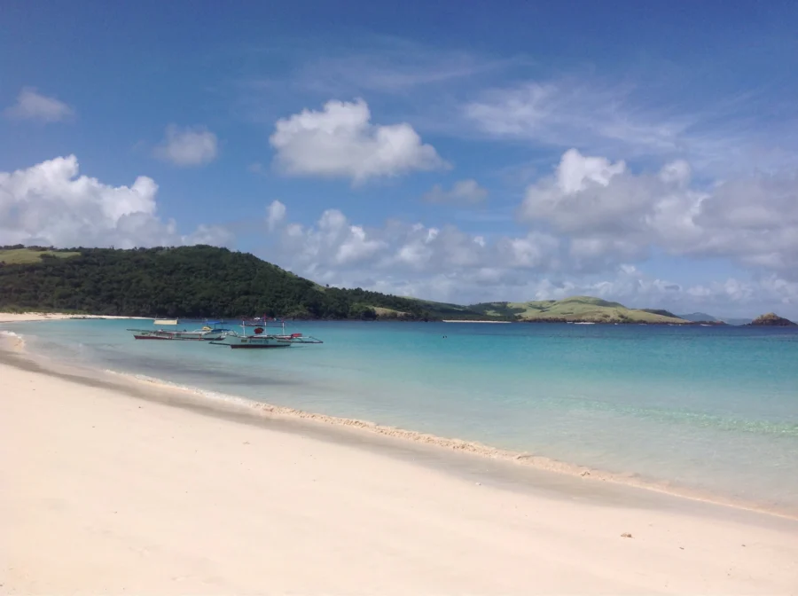 Calaguas Beach white-sand bay with turquoise water and outrigger boats in the Philippines.