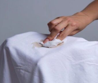 Hand blotting a coffee stain on a white t-shirt.