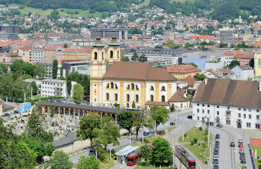 Scenic view of Wilten, Innsbruck, featuring a church surrounded by lush trees in an urban setting.