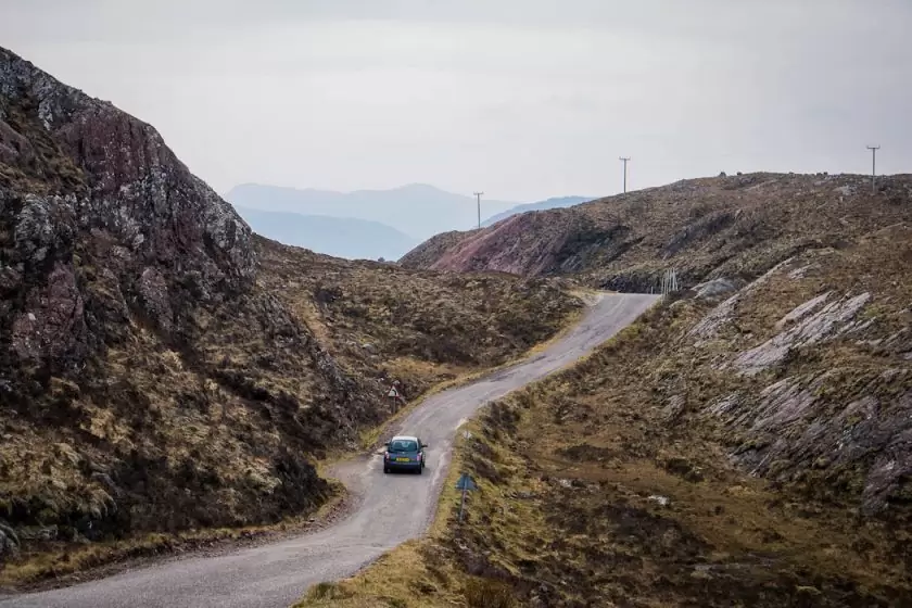 Car on winding road through rugged hills in remote natural landscape.