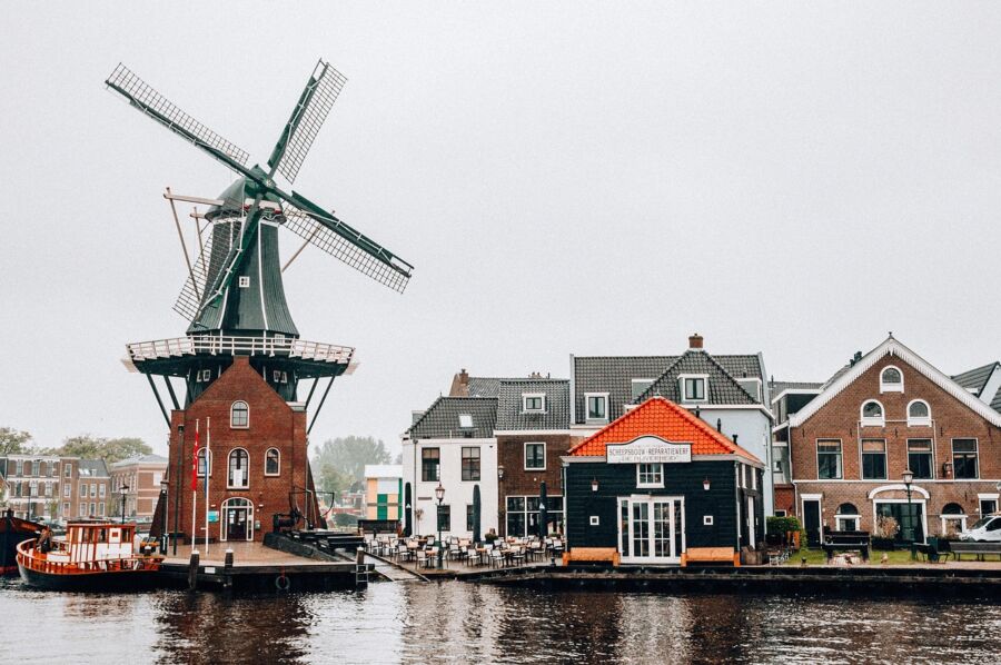 Traditional Dutch windmill by canal with boat and historic architecture in picturesque setting.