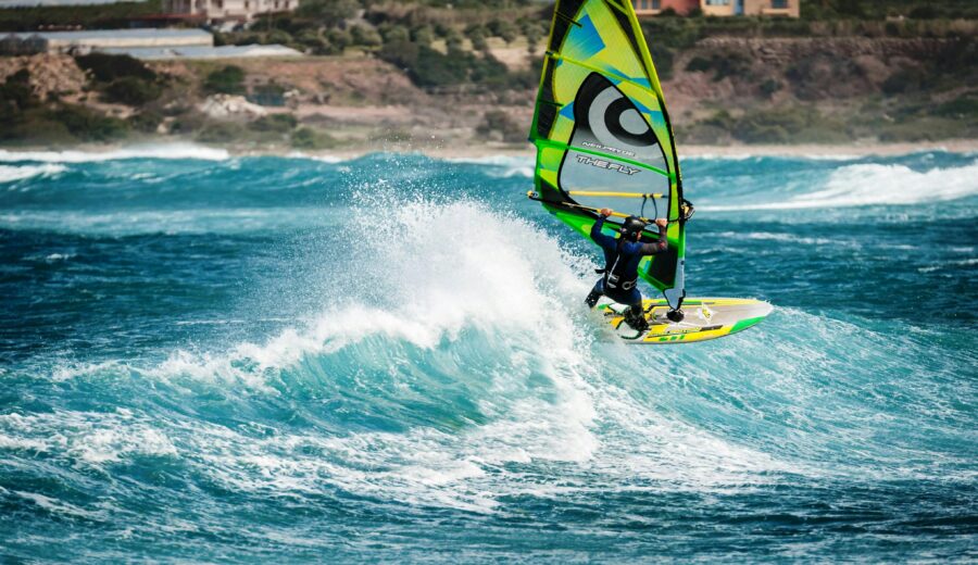 Windsurfer jumps on ocean waves with colorful sail, showing skill and excitement.