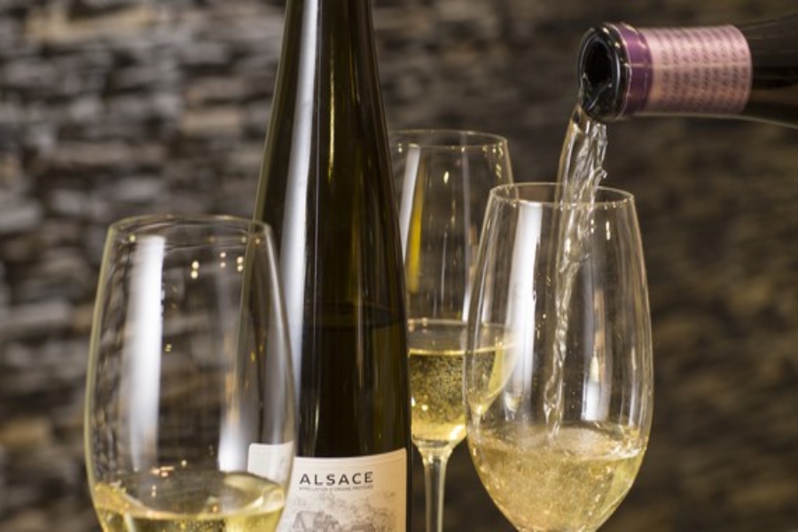 Alsace white wine bottle pouring into three stemmed glasses.