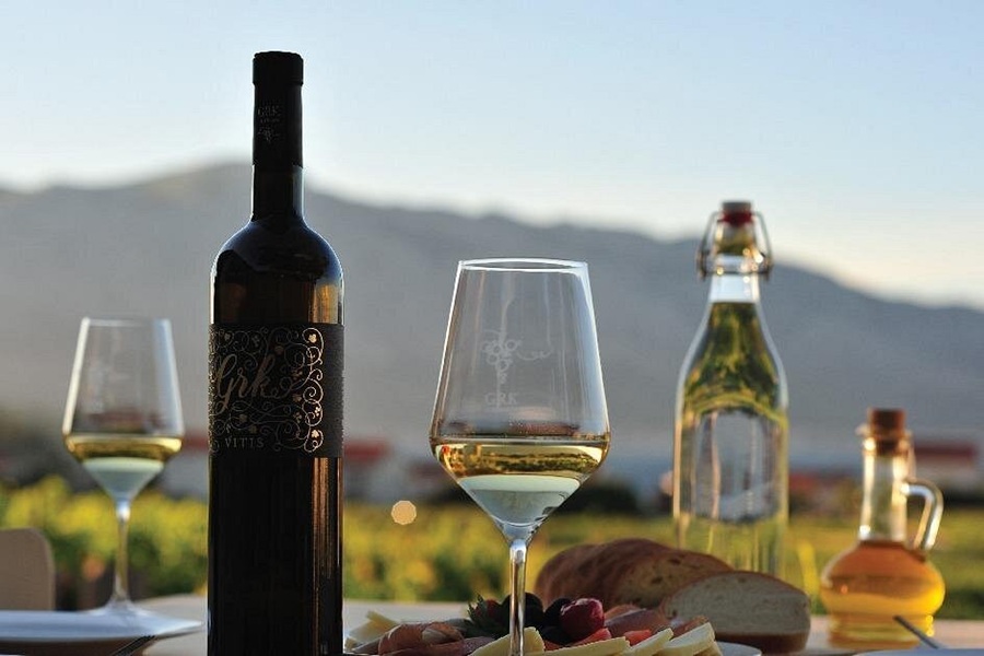 Korčula wine tasting with wine glass, bottle, antipasti, and vineyard view.