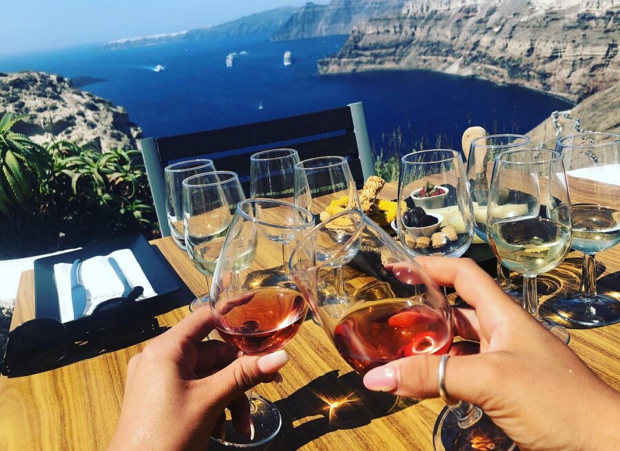 Santorini terrace wine tasting with caldera view, featuring glasses and gourmet food.