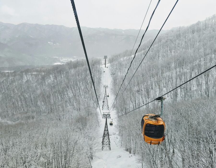 Orange cable car in snowy winter landscape with mountains, trees, and metal towers.