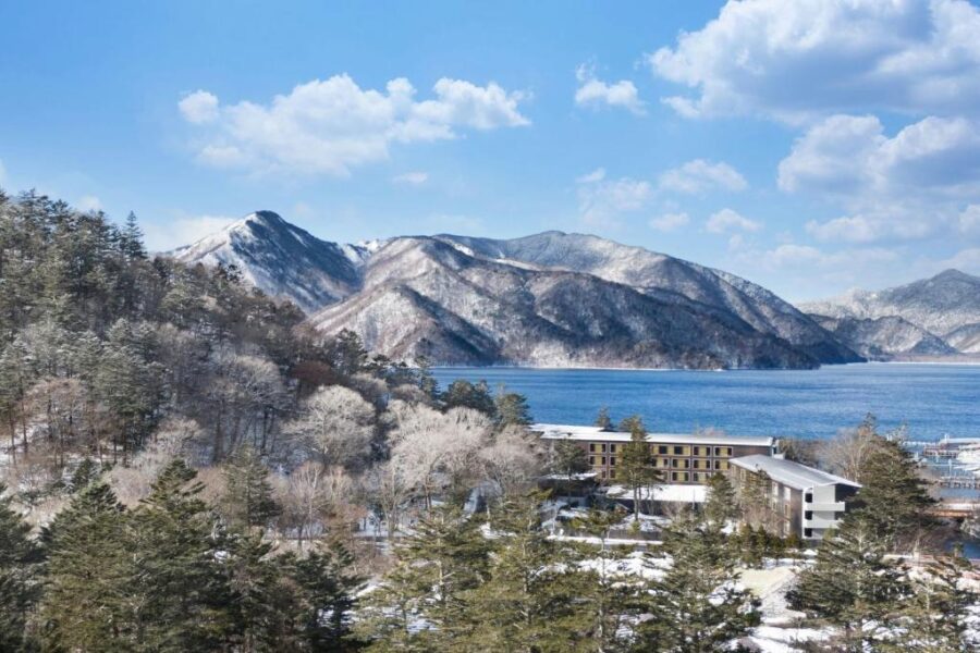 Luxury winter lake resort with snow-covered mountains, evergreen forest, and tranquil blue water views.
