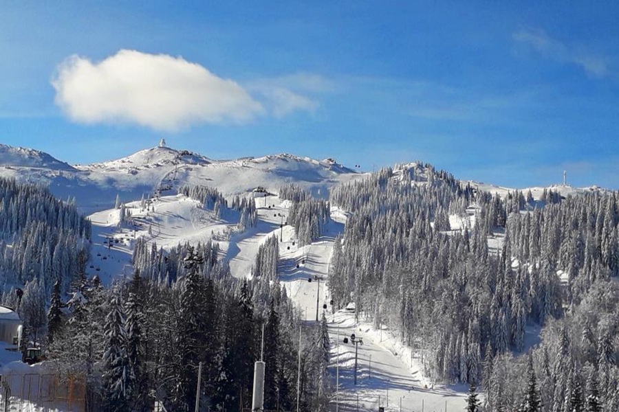 Snow-covered Mount Jahorina, ski trails, evergreen trees under clear blue sky.