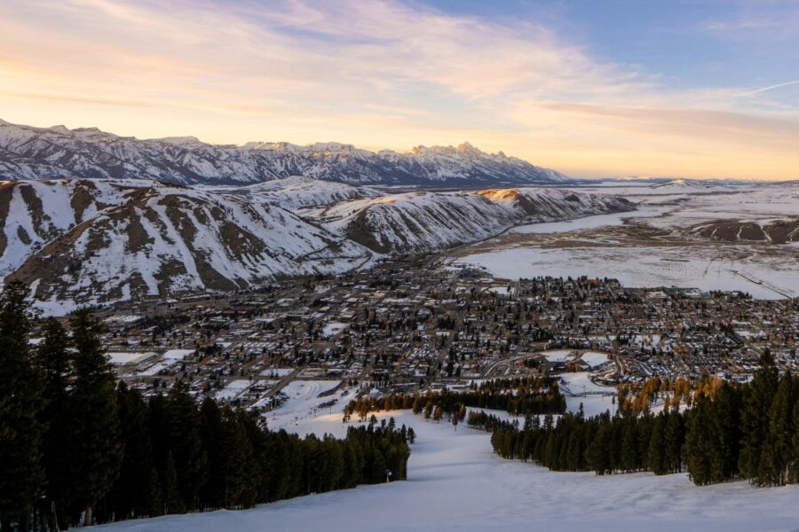 Panoramic winter landscape with snowy mountains, pine trees, and a picturesque town.