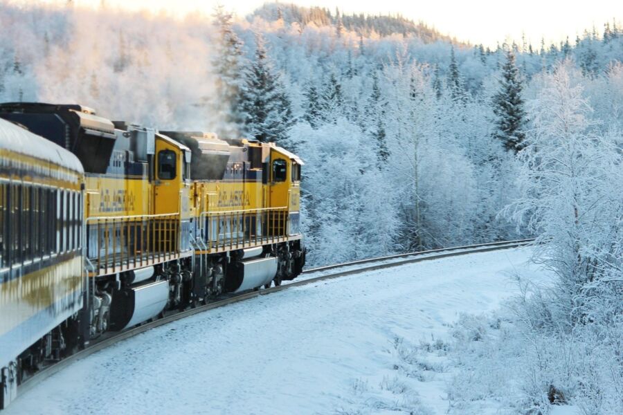 Yellow train travels through snowy winter landscape with frosty trees and rolling hills.