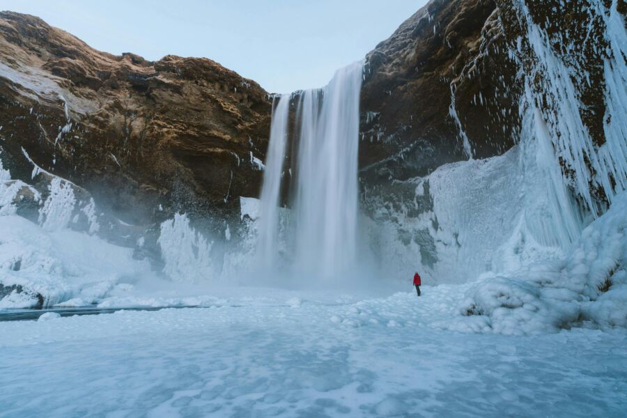 Majestic frozen waterfall in winter landscape with icy cliffs and solitary figure.