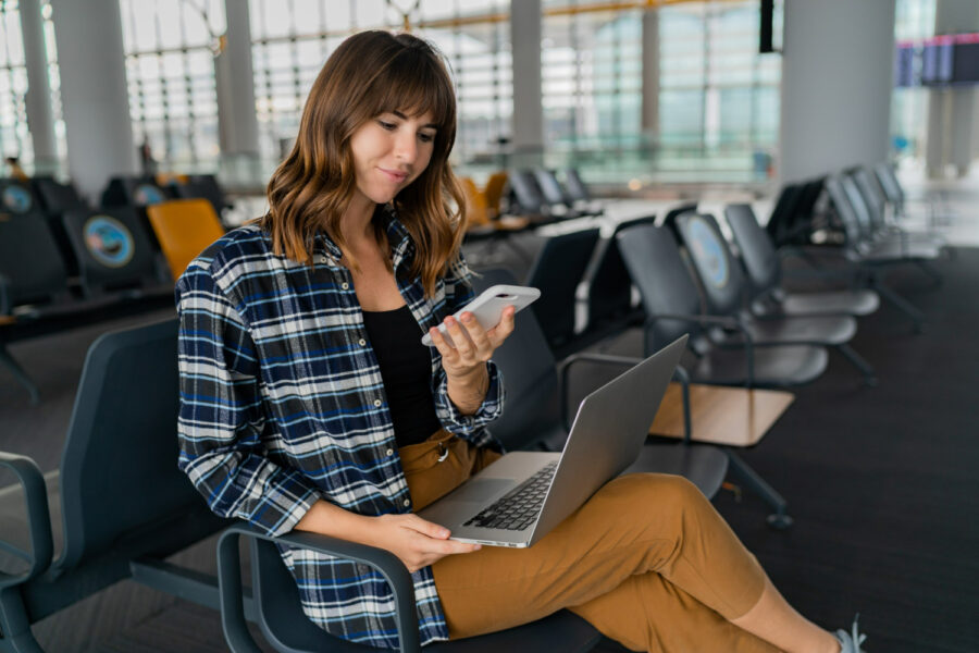 Woman using laptop and smartphone in airport waiting area.