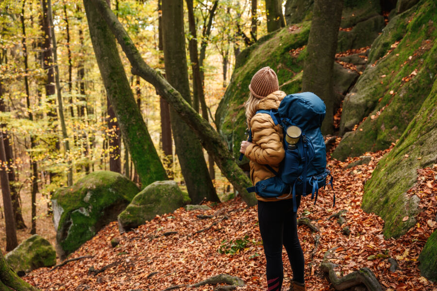 Woman with a backpack hiking in a picturesque autumn forest, enjoying the beauty of the woodland landscape