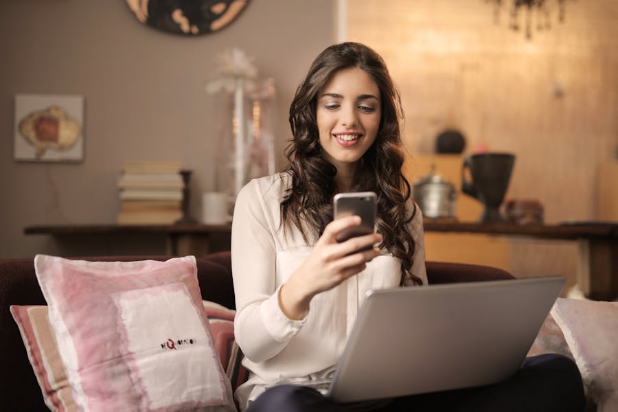 Woman on sofa with laptop and smartphone, working from home scene.
