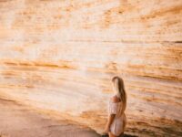 Woman contemplating sandstone rock wall on serene beach.