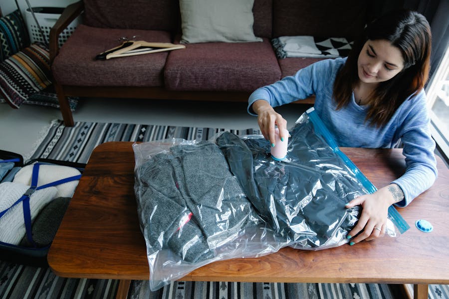 Woman using vacuum storage bag to compress clothes for space saving home organization.