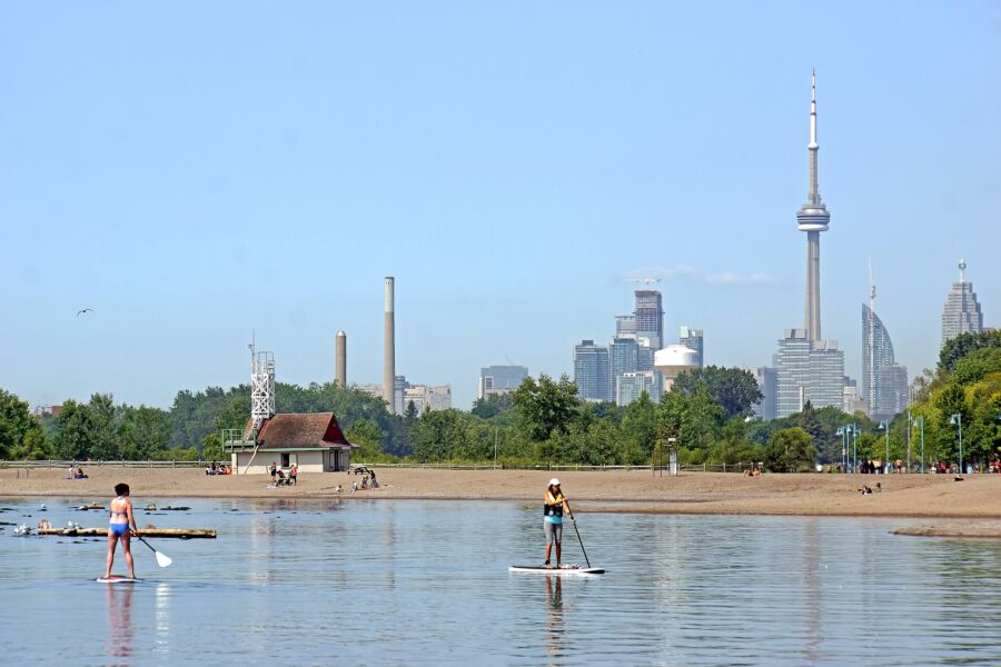 Several individuals paddle board on the calm waters of Woodbine Beach, Toronto, Canada, surrounded by a scenic landscape.
