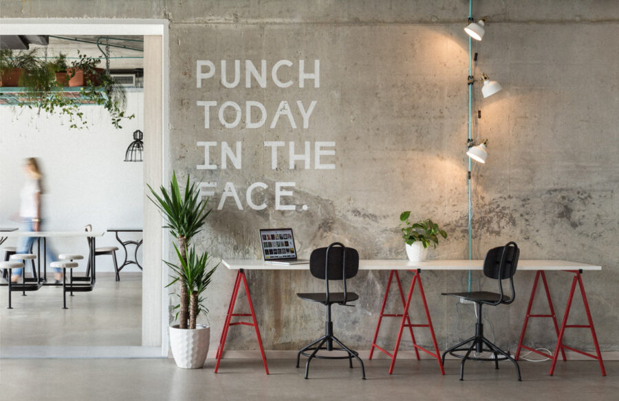 Modern workspace with motivational text, sleek furniture, greenery, and abundant natural light.
