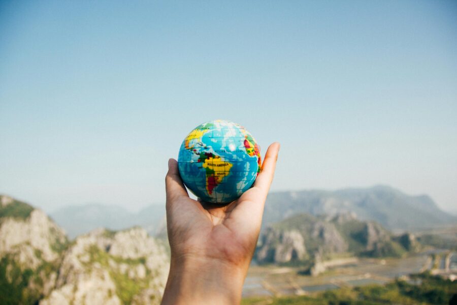 Hand holding globe against a mountain backdrop, symbolizing global unity and environmental stewardship.