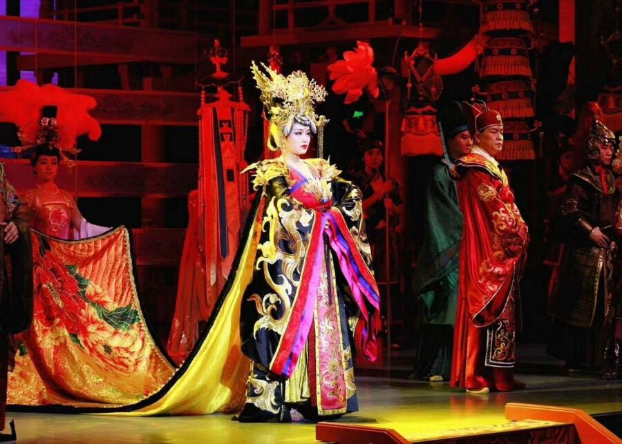 Woman in a vibrant costume stands on stage alongside fellow performers at the Xian Tang Dynasty Dance Show.